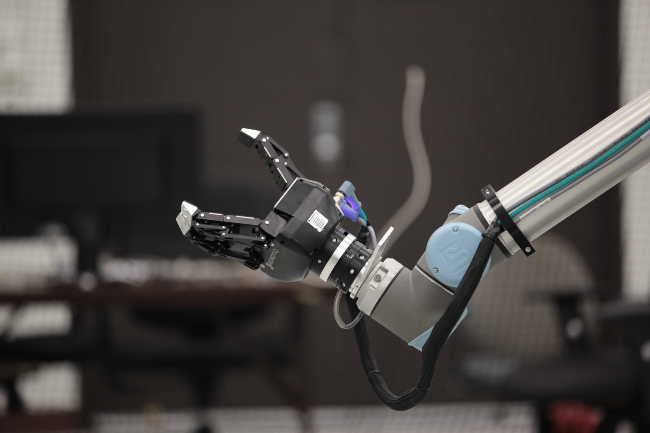 A Universal Robots arm fitted with a Robotiq gripper, reaching into the lab workspace.